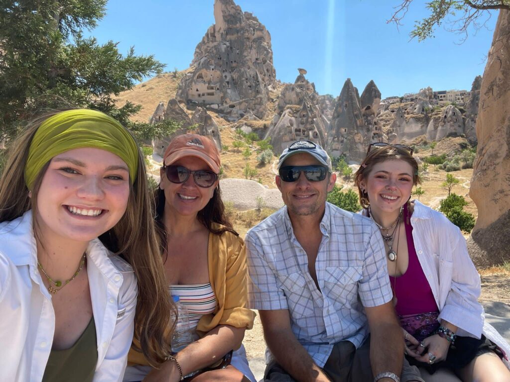 Stefanie and her family standing in front of the ancient cave dwellings of Cappadocia, Turkey, with unique rock formations and historic charm in the background.
